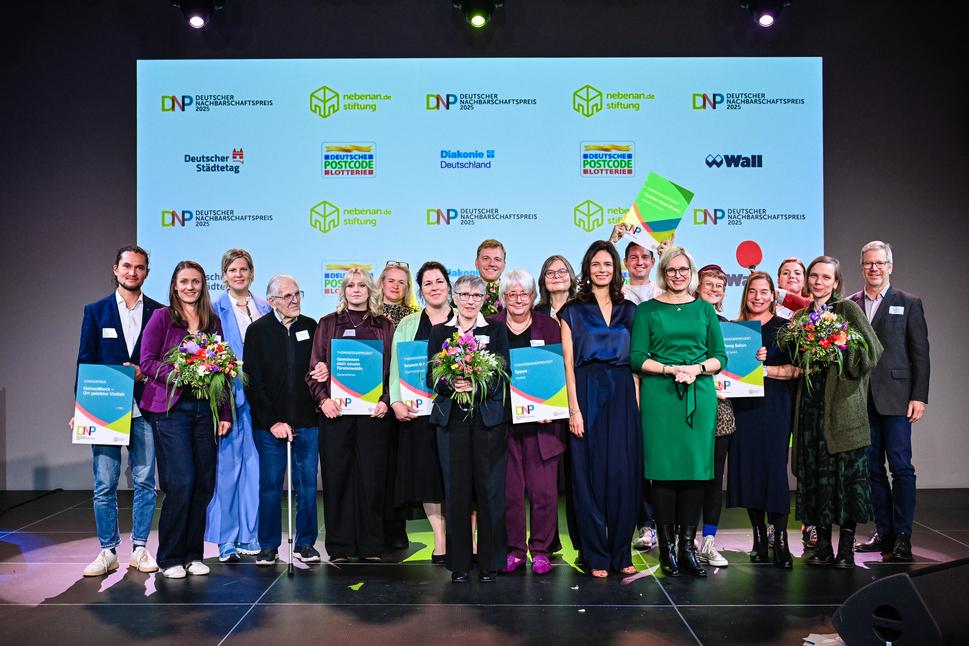 Eine Gruppe von etwa 20 Menschen steht auf einer Bühne. Es sind Preisträger des Deutschen Nachbarschaftspreises. Einige halten Blumensträuße in den Händen, andere Urkunden.