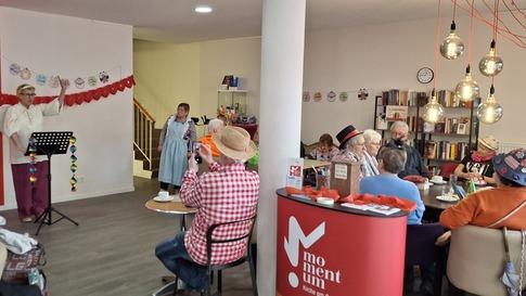 Begegnungscafé momentum: Menschen sind ein einem feierlich dekorierten Raum zusammen gekommen, um einer Person zuzuhören, die Musik macht.