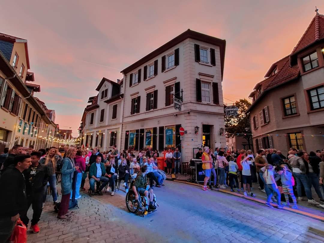 Kultur- und Begegnungsstätte Hamburger Tor: vor einem Gebäude stehen abends bei untergehender Sonne auf einem Straßenfest viele Leute auf der Straße.