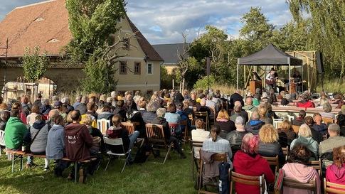 Eine große Gruppe Menschen sitzt im Freien an Tafeln im Kulturhof Kleinmecka.